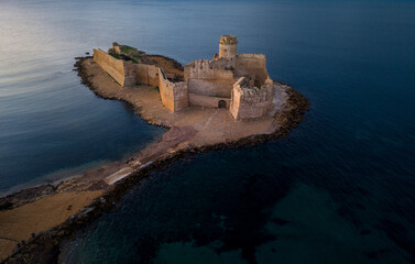 Historic castle ruins on a coastal island surrounded by calm waters in the evening light