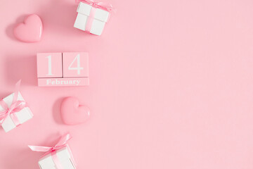 Pink festive valentine's day background. Wooden calendar for February 14 on pink background. Valentine's day concept, gift with satin bow and pink glossy heart. Top view, flat lay.