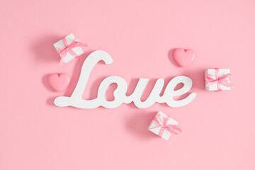 On a pink background, the word LOVE surrounded by hearts and presents. Valentine's day or Wedding romantic concept. Top view, flat lay, copy space