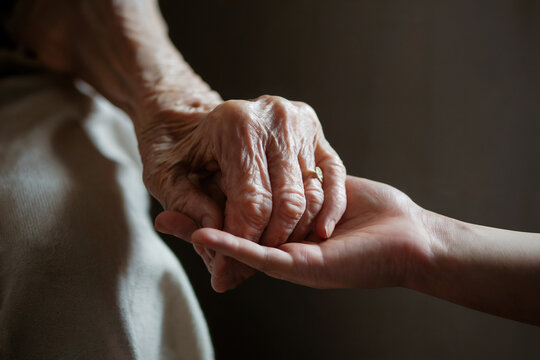 Mano de una anciana sujetando una mano de una persona joven. Generado con IA