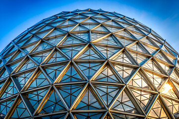 A geometric glass dome structure with a vibrant blue sky reflecting on its surface, showcasing modern architectural design.