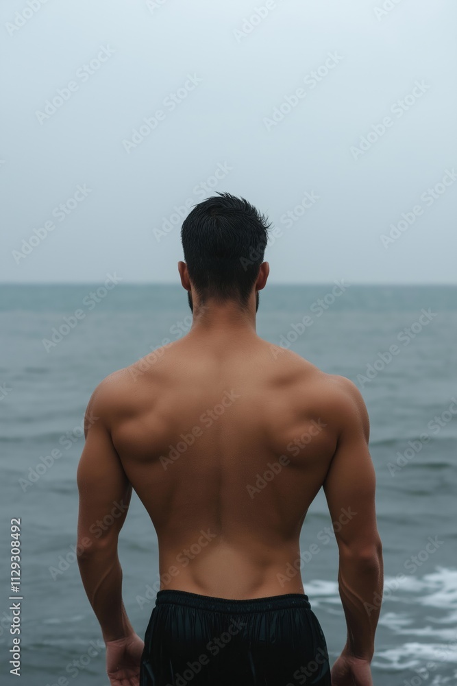Poster a man with a muscular back is standing on a beach with the ocean in the background. the man is in a 