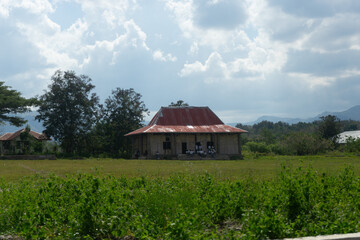 Obraz premium A rustic house sits in a lush green field under a cloudy sky.