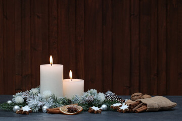 Weihnachtshintergrund: Weiße Kerzen mit Weihnachtsschmuck, Äpfeln, Zimtsternen und Tannenzweigen vor einem Holzhintergrund mit Platz für Text.