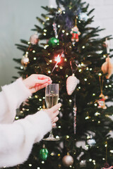 A wonderfully festive scene showcasing a person joyfully holding a glass of champagne near a beautifully adorned tree