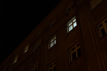 A tall and striking building adorned with an abundance of windows is beautifully lit up at night, casting a warm glow in the darkness