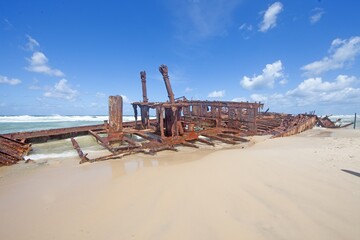 Shipwreck on Fraser Island with waves, sandy beach, and vibrant blue sky