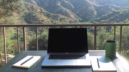 A minimalistic scene featuring a blank laptop screen on a table with notebooks and a mug against a scenic mountain backdrop