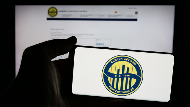 Stuttgart, Germany - 11-25-2024: Person holding mobile phone with logo of General Statistics Office of Vietnam (GSO) on screen in front of web page. Focus on phone display.