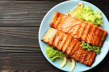Delicious grilled salmon fillets with lettuce and lemon on wooden table, top view. Space for text