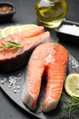 Fresh raw salmon steaks with salt, lemon and rosemary on dark textured table, closeup