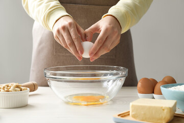 Making cashew cookies. Woman adding egg into bowl at white wooden table, closeup
