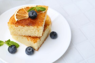 Pieces of delicious semolina cake with blueberries and orange slices on white tiled table, closeup