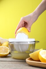 Woman with lemon using juicer at wooden table, closeup