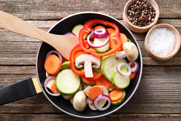 Frying pan with mix of fresh vegetables, mushrooms and spices on wooden table, flat lay