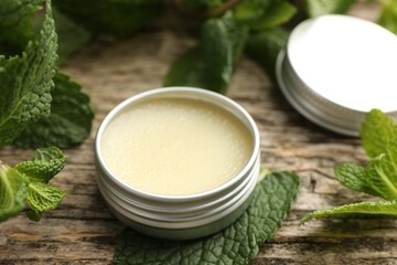 Natural lip balm and mint leaves on wooden background, closeup