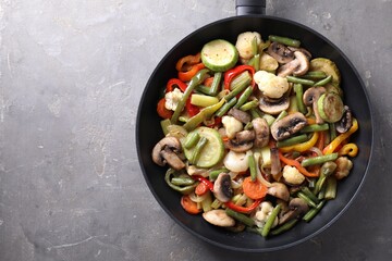 Different vegetables and mushrooms in frying pan on grey table, top view. Space for text