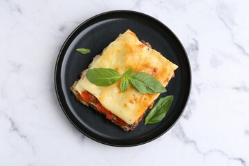 Delicious cooked lasagna with basil on white marble table, top view