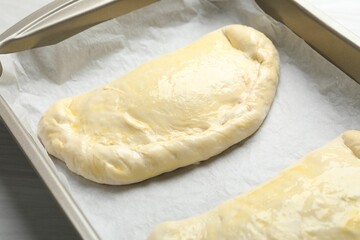 Uncooked calzone pizza in baking dish on white wooden table, closeup