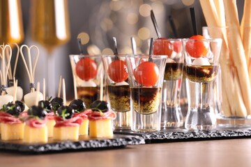 Many different tasty canapes on wooden table against blurred lights