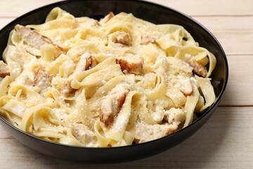 Tasty Alfredo pasta with chicken on light wooden table, closeup