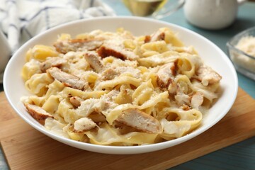 Tasty Alfredo pasta with chicken on light blue wooden table, closeup