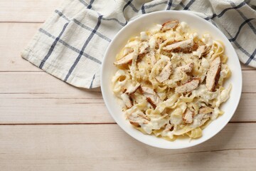 Tasty Alfredo pasta with chicken on light wooden table, top view. Space for text