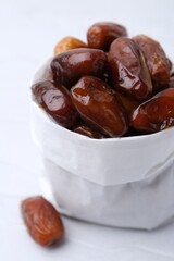 Tasty sweet dried dates in paper bag on white table, closeup