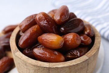 Tasty dried dates in wooden bowl on white table, closeup