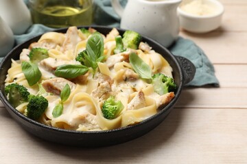 Delicious pasta Alfredo with chicken, cheese, creamy sauce, broccoli and basil on wooden table, closeup