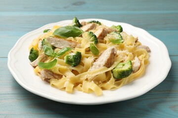 Delicious pasta Alfredo with chicken, cheese, broccoli and basil on light blue wooden table, closeup