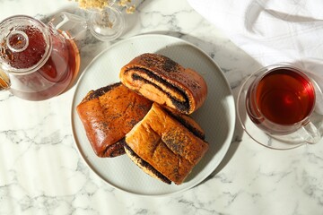 Tasty buns with poppy seeds served with tea on white marble table, flat lay