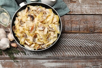 Flat lay composition with tasty Alfredo pasta with chicken and mushrooms in frying pan on wooden table, space for text