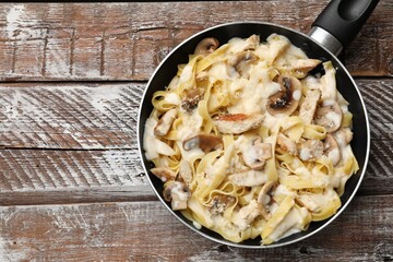 Tasty Alfredo pasta with chicken and mushrooms in frying pan on wooden table, top view. Space for text