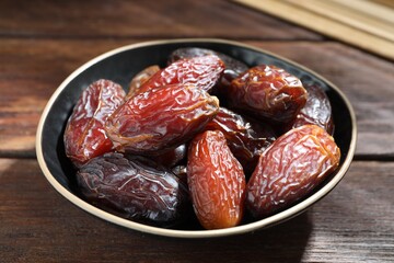 Many tasty dried dates in bowl on wooden table, closeup