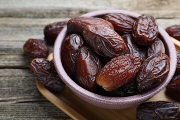 Many tasty dried dates in bowl on wooden table, closeup