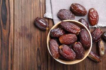Many tasty dried dates in bowl on wooden table, top view. Space for text