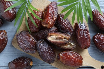 Many tasty dried dates and leaves on blue wooden table, top view