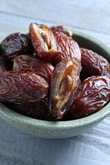 Many tasty dried dates in bowl on blue wooden table, closeup