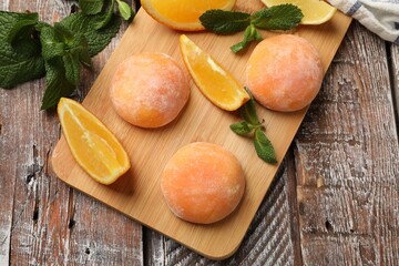 Board with tasty mochi, cut orange and mint on wooden table, flat lay