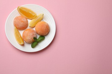 Plate with tasty mochi, cut orange and mint on pink table, top view. Space for text