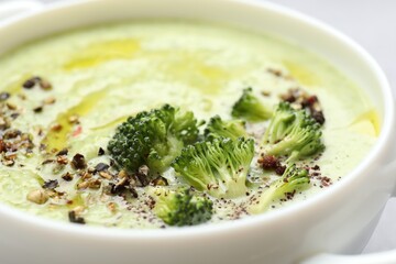 Delicious broccoli cream soup in bowl on light table, closeup