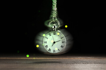 Hypnosis session. Vintage pocket watch swinging on black background, motion blur effect. Magic...
