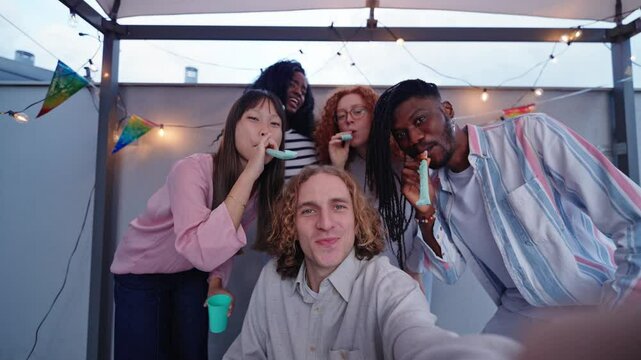 Multiethnic friends taking group selfie while blowing party blowers