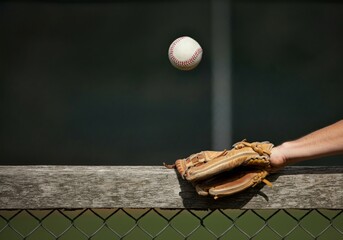 A baseball mid-air, just above a glove reaching over an outfield fence