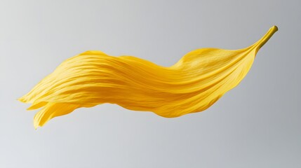 A yellow sunflower petal floating mid-air over a soft gray background.