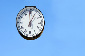 Street clock with Roman numerals, blue clear sky