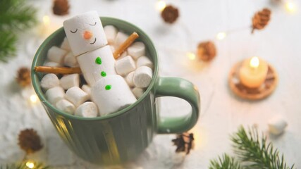 cute christmas card, Cheerful marshmallow snowman relaxes in a green mug of hot chocolate, surrounded by mini marshmallows, cinnamon sticks, and festive christmas lights, creating cozy holiday scene - Powered by Adobe