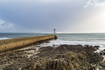 Au bout du môle, le phare du Raoulic se dresse majestueusement, tandis qu'au premier plan, une...