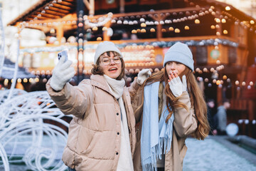Friends enjoying winter festivities while taking selfies at a festive market with lights and decorations